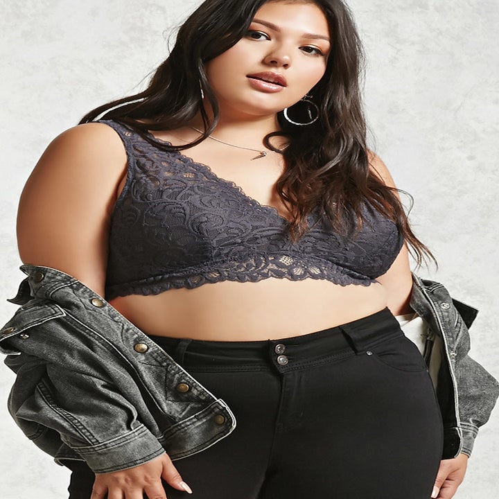 a model wearing a dark gray lace bralette with black jeans and a gray denim jacket