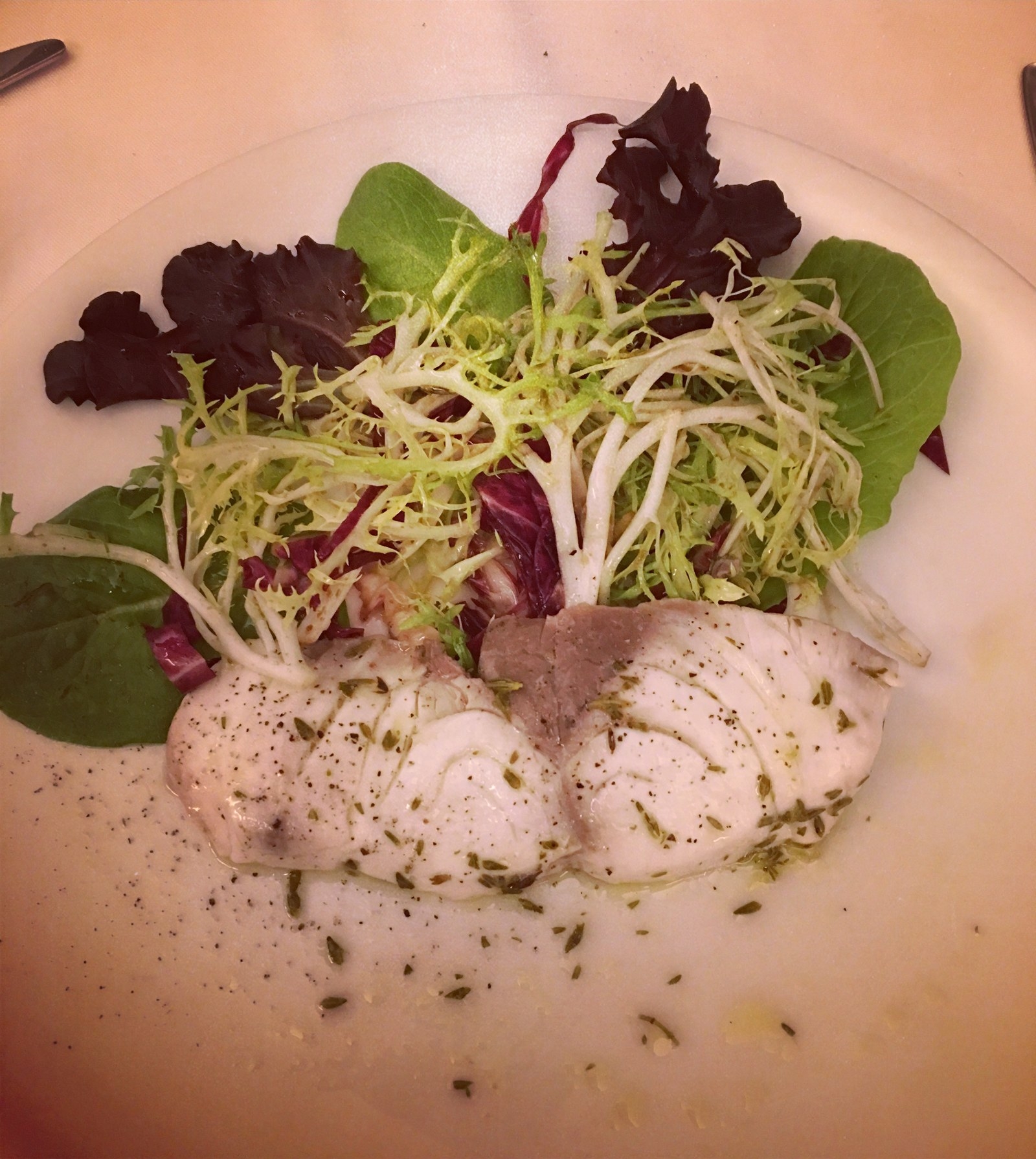 Light and healthy sliced filet of broiled wild bass is served over a salad of radicchio and frisee with a drizzle of olive oil