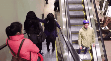 People on an escalator going down, and one person standing backward on an elevator going up