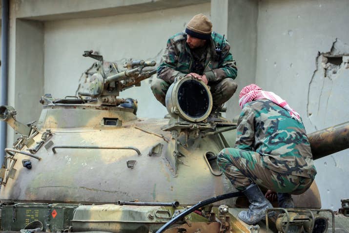 Members of the Syrian government forces sit over the turret of a tank.
