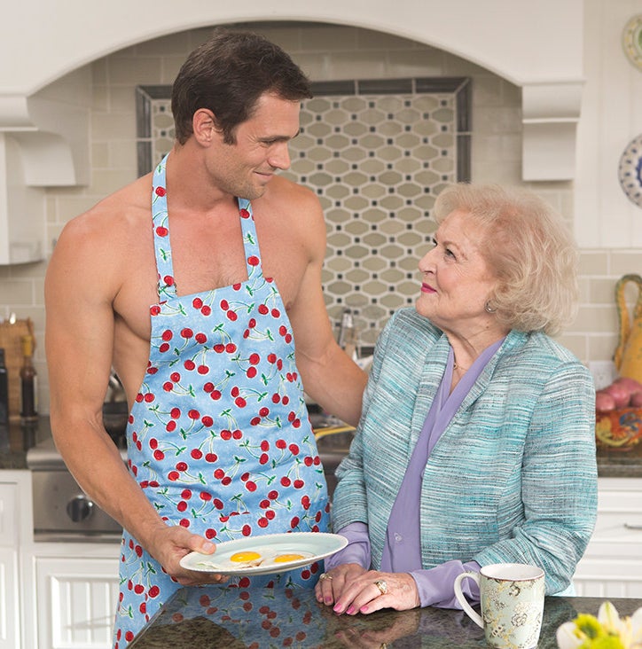 Betty smiles at a bare-chested man wearing a kitchen apron and holding a plate of eggs sunny side up
