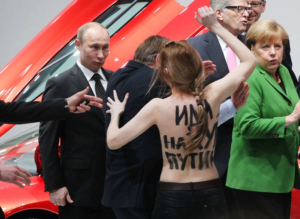 Putin and German Chancellor Angela Merkel react as an activist from the Ukrainian womens' rights group Femen protests during a visit to an industrial exhibition in Hannover, Germany, on April 8, 2013.