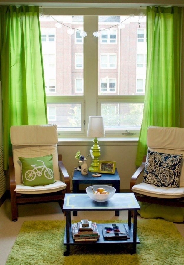 A large window with green curtains, a green area rug, and green accents on chairs and tables