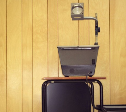 A projector on a desk in front of a wood paneled wall