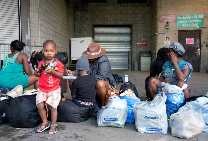 A group of Haitian asylum seekers sit with shopping bags outside the Olympic Stadium in Montreal.