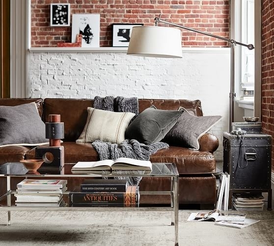 a brown leather sofa in a living room with assorted pillows and blankets thrown on it