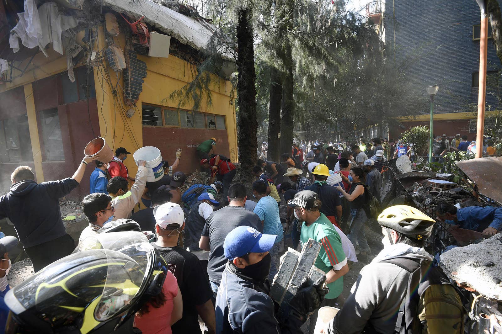 Rescuers and volunteers remove rubble and debris from a flattened building in search of survivors.