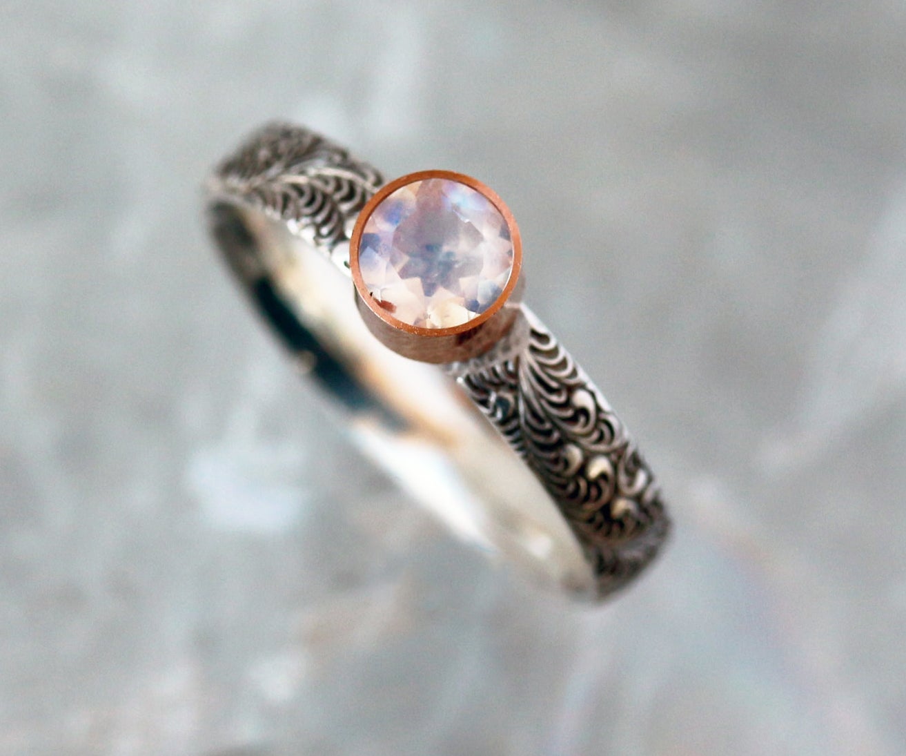 silver band with black worly design with round moonstone embedded in copper 