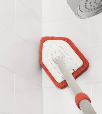 the scubber cleaning a high corner of a tile shower