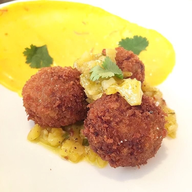 Three balls of battered and deep-fried oxtail croquetas are placed on top of chili and mango chutney with creamy saffron aioli and cilantro. The croquetas have the perfect, crispy exterior with tender, buttery oxtail meat inside. The sweet and spicy chutney balances out the overall flavor.