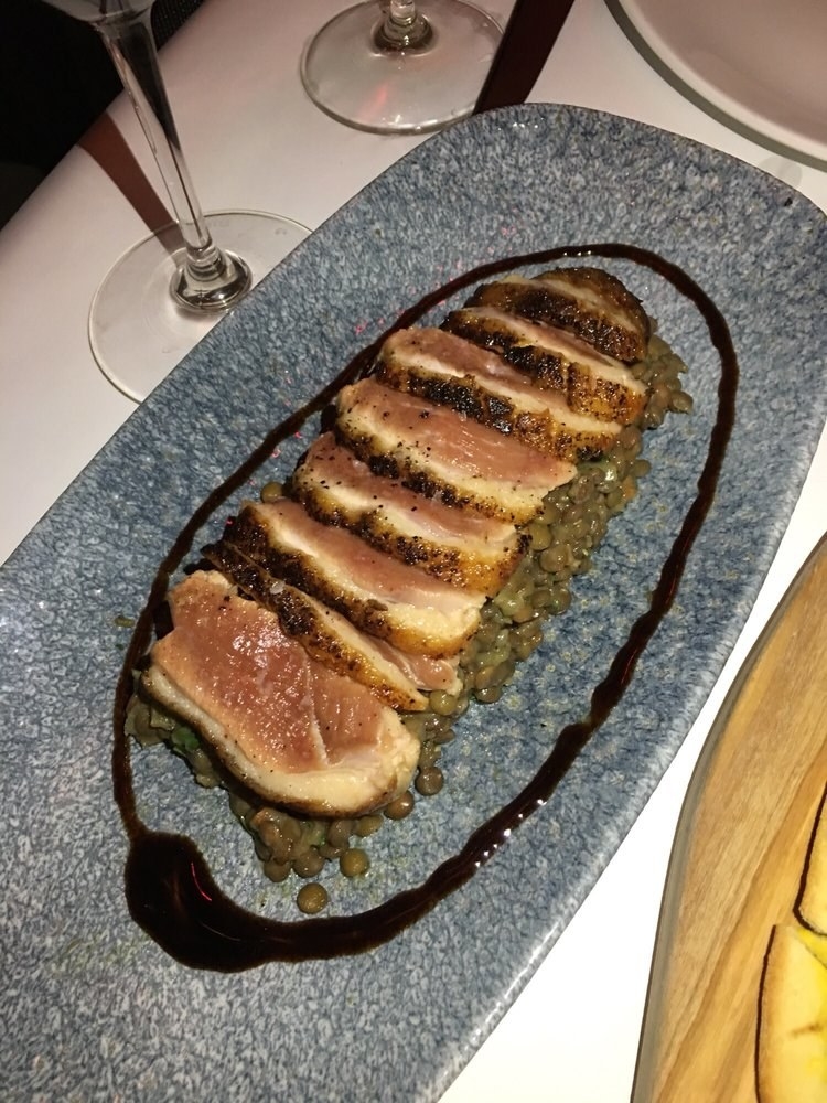 Tender, medium-rare slices of duck breast is served on top of cooked lentils with pearl onions. The duck is served with thick balsamic vinegar to add additional flavor to the dish.
