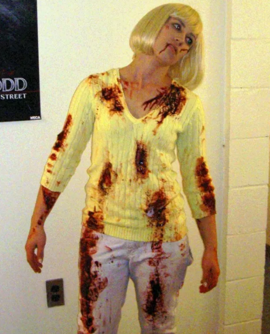 Woman in platinum wig with &quot;blood&quot; spattered on her sweater and pants