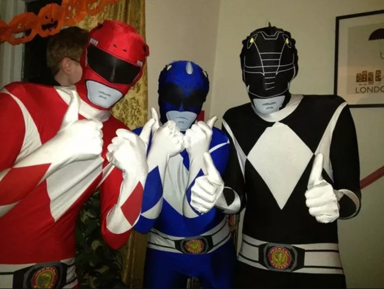 Three people giving a thumbs-up and wearing different-colored superhero costumes