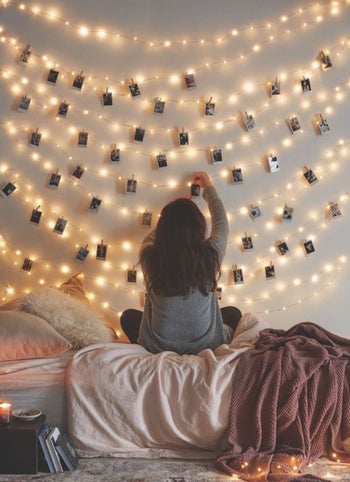 someone hanging instant photos on the string lights as they hang on the wall