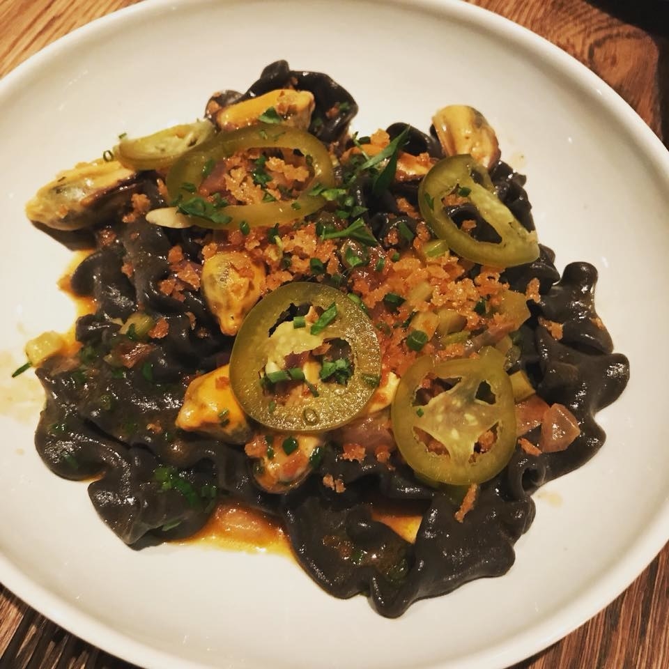 Flat, wide ribbon-shaped pasta colored black with squid ink is tossed in rich smoked mussel liquer and sofrito, and topped with pickled jalapeños, crispy breadcrumbs, and fresh herbs in this delectable dish.
