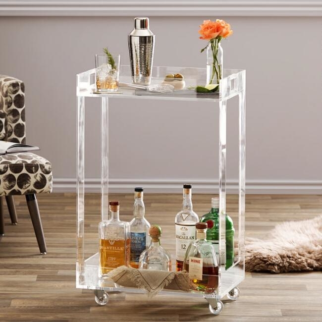 Acrylic bar cart with bottles, shakers, glasses, and flowers on it