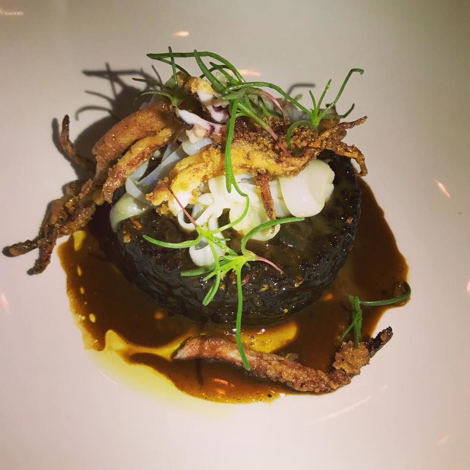 The crispy black sepia rice is topped with seared scallop and flash-fried calamari, and served over rich, savory sauce of almond ajo blanco, olive oil, and piquillo pepper.