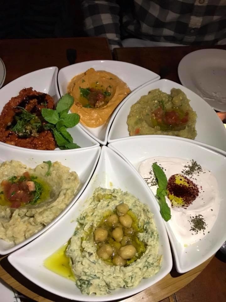 Try a sample of all the best-selling vegetarian dips. The platter includes, clockwise from top, Spicy Hummus (puréed chickpeas with tahini sauce, lemon juice mixed with capsicum), Saltet Al Raheb (chopped char-grilled eggplant with tomatoes, bell peppers, garlic & extra virgin olive oil), Labne (classic Levantine cream cheese & extra virgin olive oil), Hummus Beiruti (puréed of chickpeas with cumin, chopped parsley, tahini & lemon juice), Baba Ghanoush (char-grilled eggplant purée with tahini & fresh lemon juice), and Muhammara (a blend of spicy & sweet pepper with walnuts & pomegranate molasses)