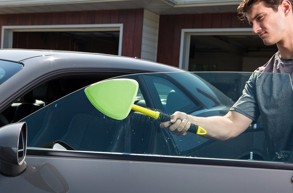 person using tool to clean their driver&#x27;s side window 
