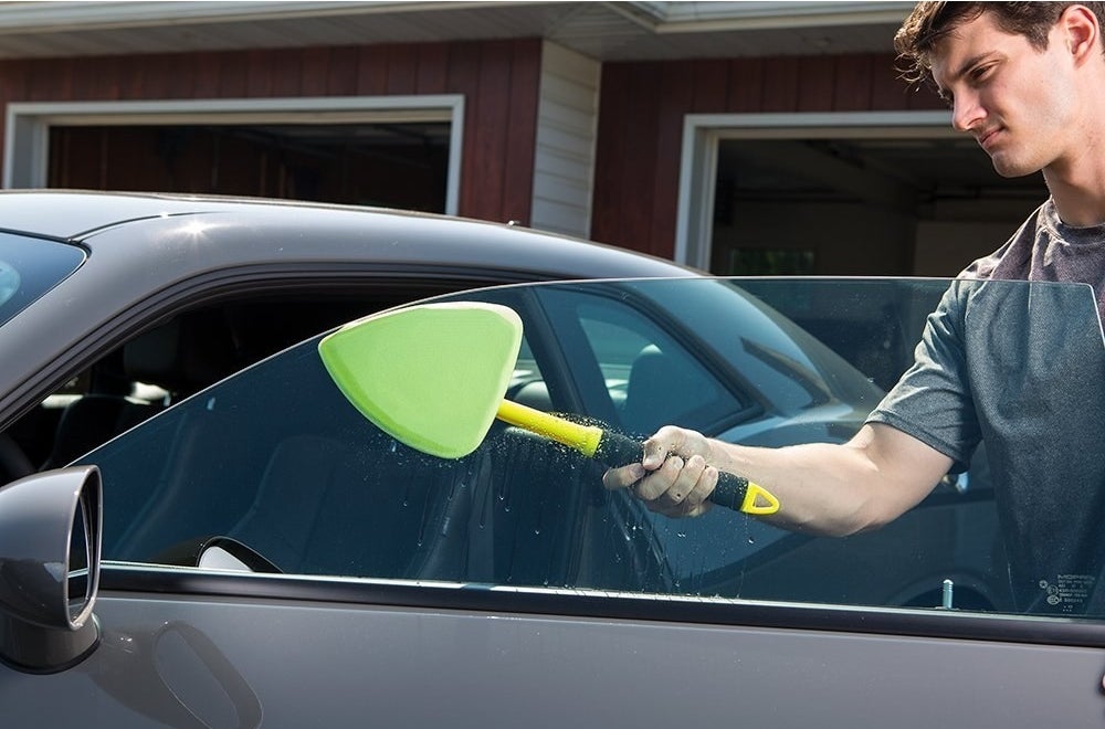 person using tool to clean their driver&#x27;s side window 