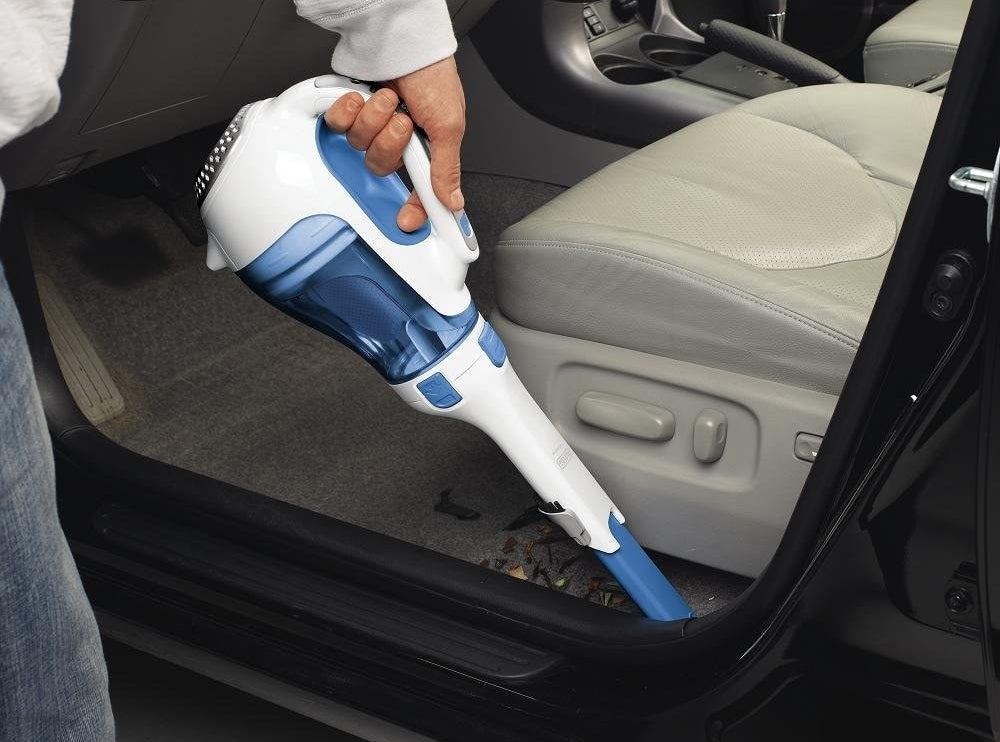 person using vacuum to clean out crevices near car door 