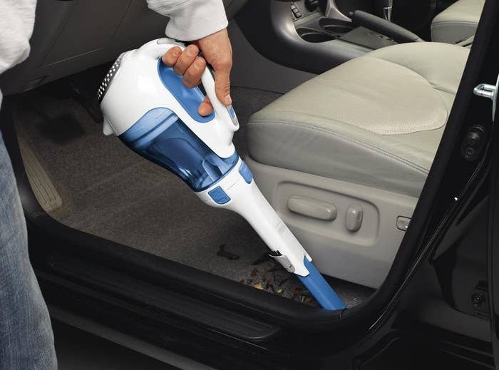 person using vacuum to clean out crevices near car door 