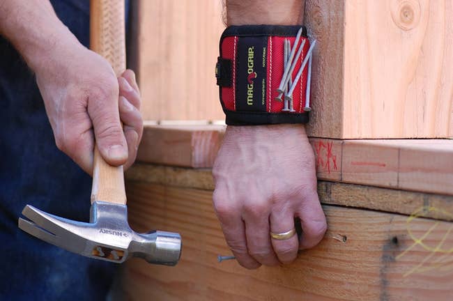 model wearing red wristband with nails stuck to it while they hammer one into wood
