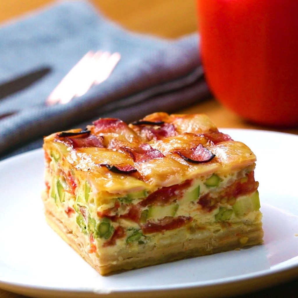 Pour 9 convivesINGRÉDIENTS4 fonds de tarte déjà prêts2 cuillères à soupe de farine2 bottes d'asperges (pour obtenir au final quelques dizaines de tronçons)400 g de haricots secs8 œufs40 g de courgette, tranchée200 g de tomate hachée30 g de mozzarella râpée (ou un autre fromage de votre goût)Une pincée de poivreUne pincée de sel240 g de crème épaisse10 tranches de jambon 15 tranches de fromagePRÉPARATION1. Préchauffer le four à 120 °C.2. Sur une surface enfarinée, découper les fonds de tarte pour les adapter à un moule carré d'environ 20 cm de côté.3. Posez les fonds de tartes les uns à côté des autres de manière à ce qu'ils se chevauchent légèrement. Avec un rouleau à pâtisserie, aplatissez les quatre fonds de tartes en insistant particulièrement sur les bords qui se chevauchent pour ne former qu'une seule grande pâte bien lisse. 4. Posez votre moule carré au milieu du fond de tarte et découpez la pâte qui dépasse en poursuivant chaque côté. Décollez et réservez les quatre morceaux de pâte qui se ne se trouvent pas dans la prolongation des côtés du plat. 5. Placez le centre du fond de tarte sur le moule carré tapissé de papier sulfurisé, de façon à ce que les bords débordent sur les côtés du moule.6. Coupez les queues de vos asperges et disposez-les verticalement tout autour du moule. Elle doivent faire la hauteur du rebord. Gardez le reste pour mettre dans l'appareil de la quiche.7. Recouvrez la bordure d'asperges en repliant le fond de tarte. Découpez l'excès. 8. Placez un carré de papier sulfurisé sur la base du fond de tarte et ajouter les pois chiches secs (ou autre).9. Faites cuire le fond de tarte pendant 40 minutes.10. Battez les œufs en omelette dans un bol.11. Ajoutez les asperges, les courgettes, les tomates, la mozzarella râpée, le poivre, le sel et la crème épaisse, en battant pour bien mélanger.12. Verser le mélange sur le fond de tarte cuit et cuire au four pendant 40 autres minutes.13. Sur une feuille de papier sulfurisé, assemblez les croisillons de jambon et de fromage.14. Posez les croisillons sur le dessus de la quiche15. Faites cuire au four pendant 20 minutes supplémentaires.16. Retirez le papier sulfurisé et découpez la quiche.17. Régalez-vous !