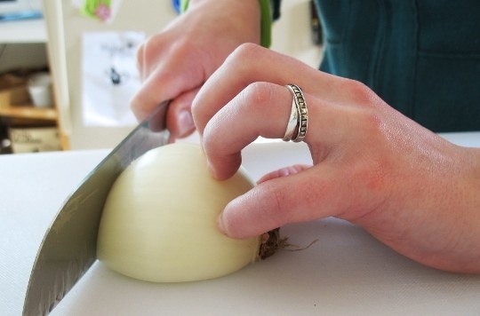 A hand holding an onion with the fingertips curled under to protect them