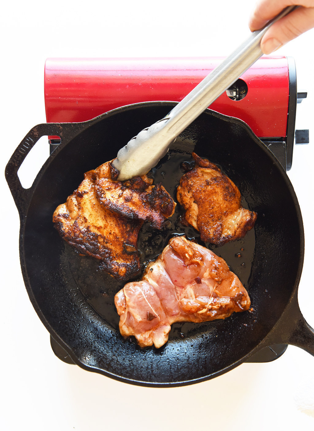 A cast iron pan with three caramelized chicken thighs