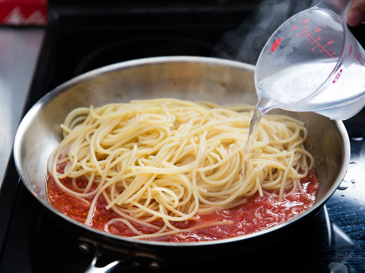 Pasta water being poured into a pan of pasta and tomato sauce