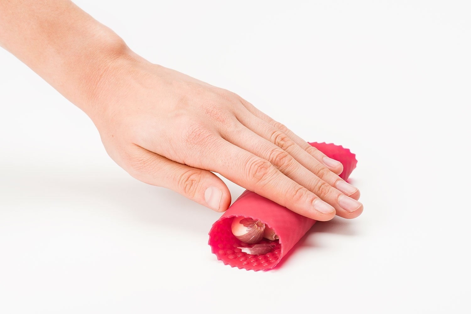 A hand rolling garlic in a silicone tube