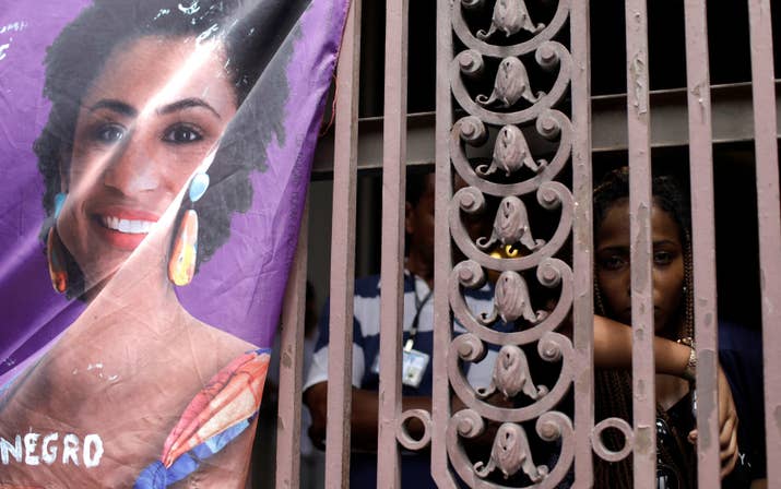 Mulher chora ao lado de cartaz com a foto da vereadora Marielle Franco