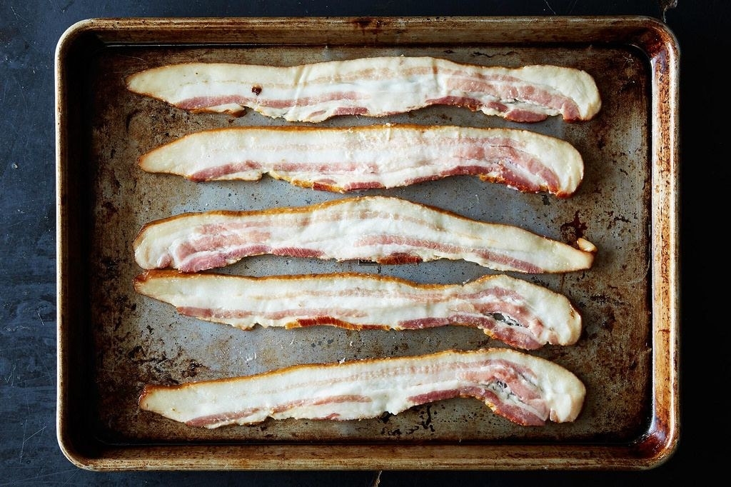 Five strips of raw bacon in a sheet pan