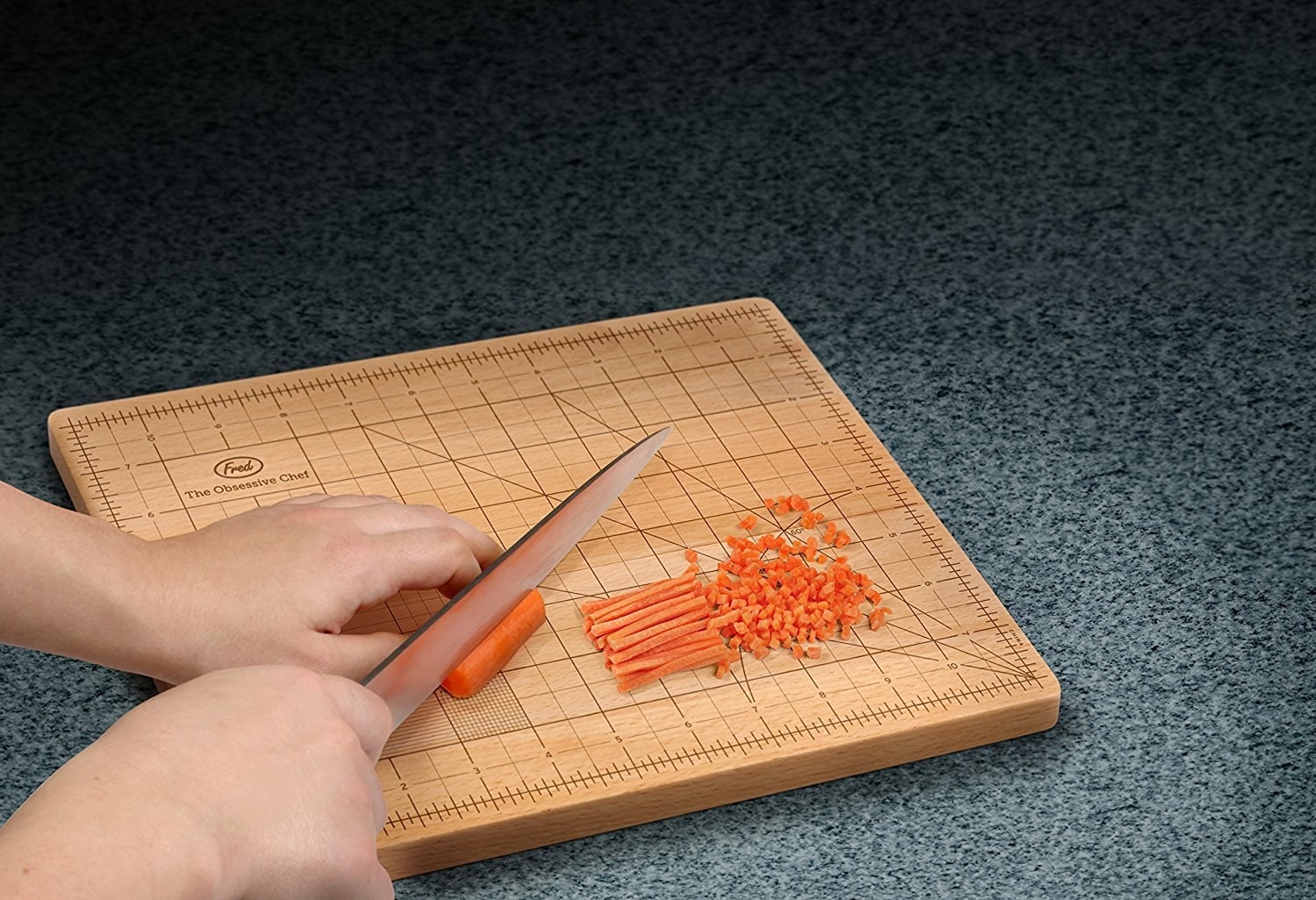 The cutting board with a grid of measurements to guide chopping, with someone julienning and small dicing a carrot on it