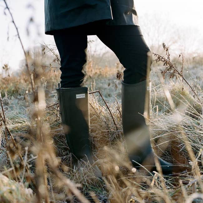 person walking through tall grass while wearing knee high Hunter boots