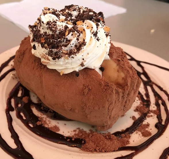 A &quot;baked potato&quot; scoop of vanilla ice cream topped with whipped cream, syrup, and powdered cocoa