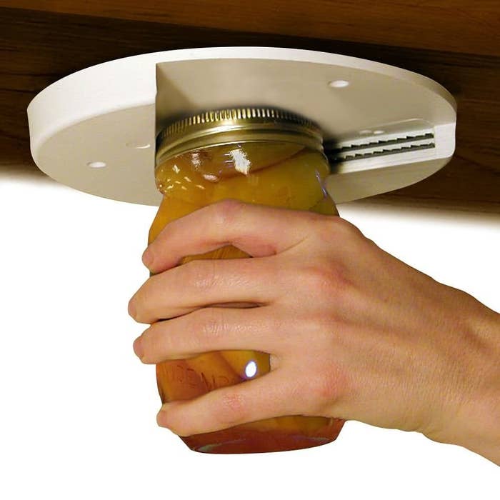 disc-shaped jar opener mounted underneath a cabinet with hand using it to open a mason jar