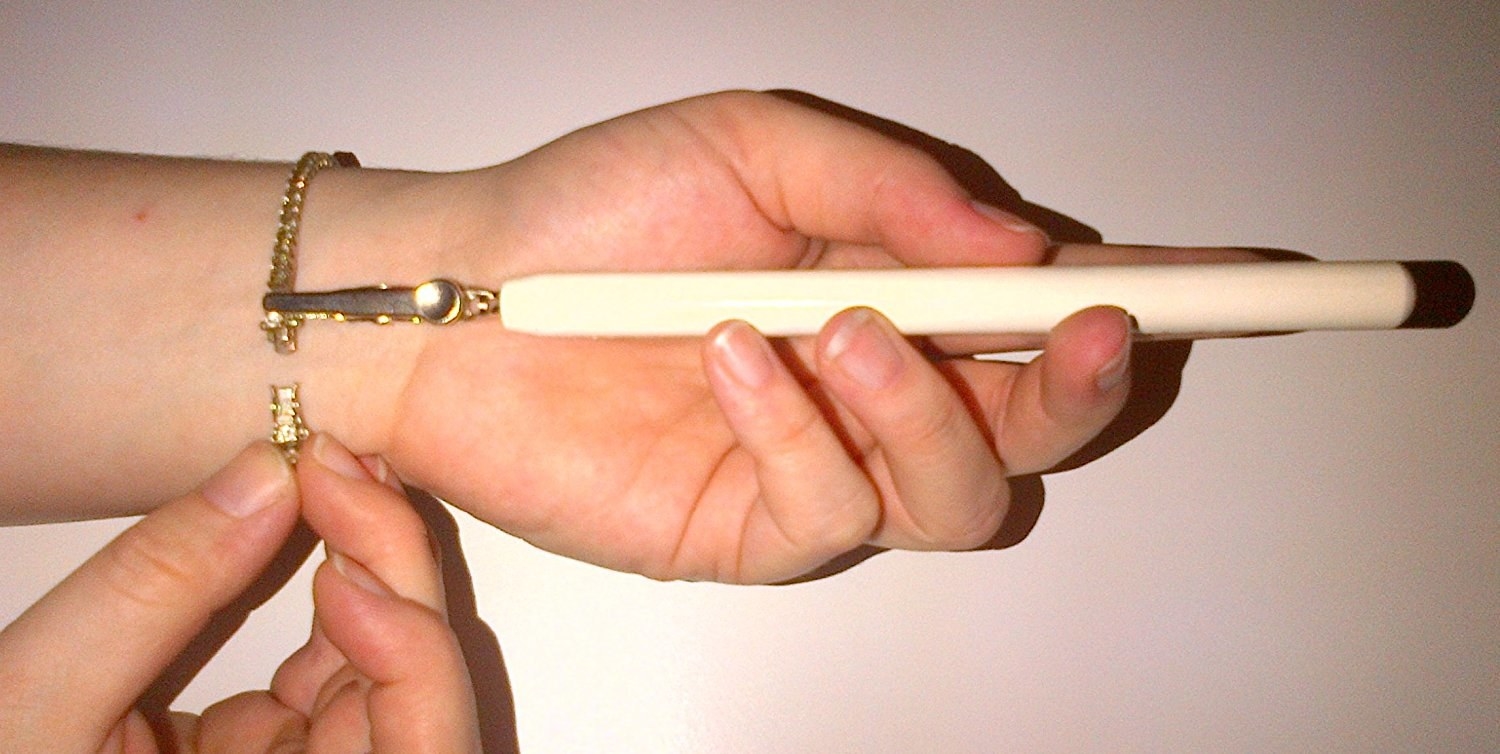 person using stick-like tool with clasp on the end of it to hold a bracelet end with one hand in place while clasping it with the other hand