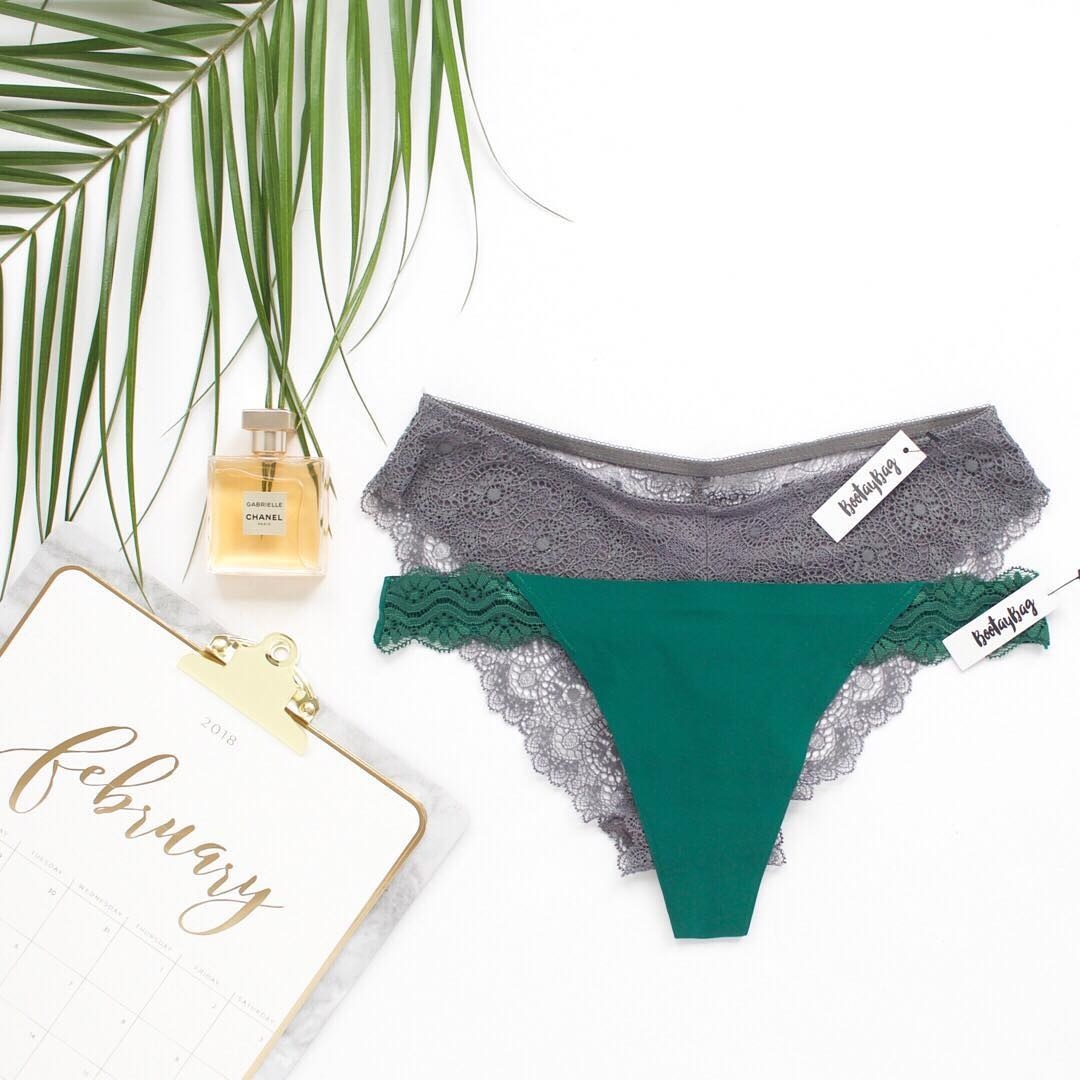 A flatlay of two pairs of undies: one grey lace bikini, one a green thong with lace sides