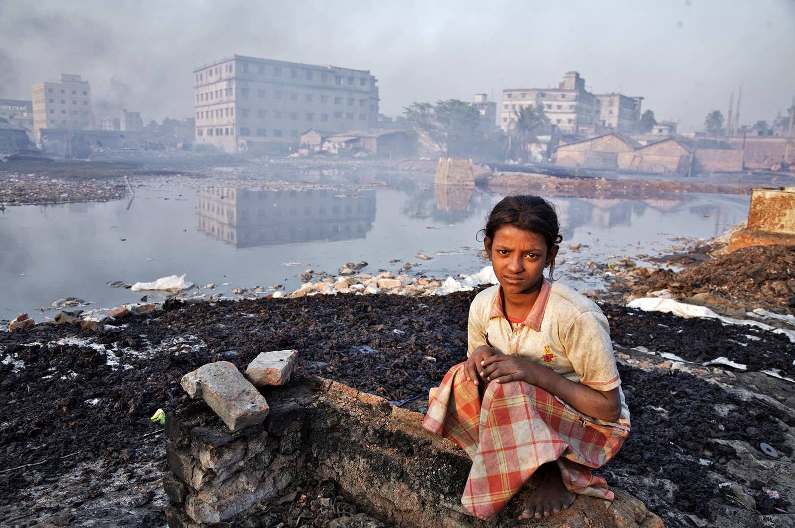 バングラデシュの首都ダッカに流れるブリガンガ川のほとりで。少女は接着剤の工場の崩れた壁の上に腰をかけている。(2007年2月20日)