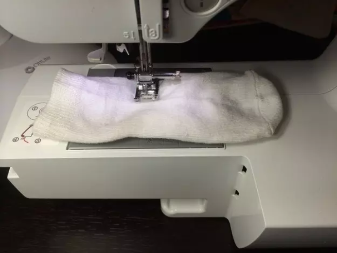 Sewing machine stitching a white sock, needle in mid-motion