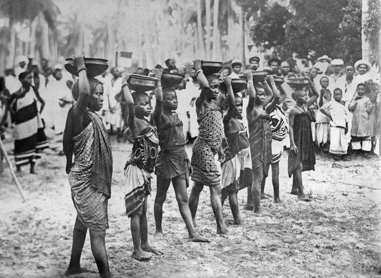 Crianças apostam corrida com jarras de água na cabeça. O vencedor era quem chegasse até o final sem derrubar o líquido.