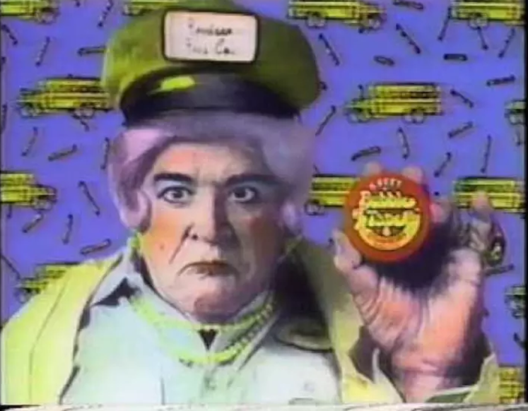 A screen shot of a old man dressed as a female school bus driver holding a rid container of Bubble Tape.
