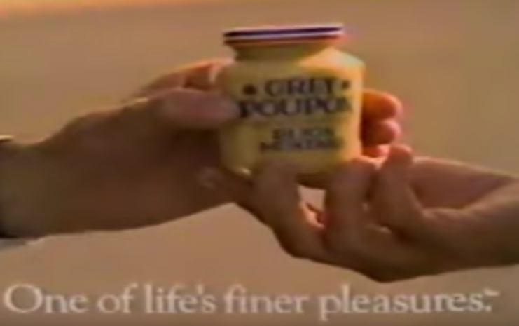 A screenshot of one handing another hand a jar of Grey Poupon.
