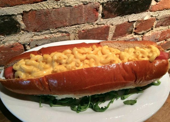 A hot dog in a bun covered in mac &#x27;n&#x27; cheese