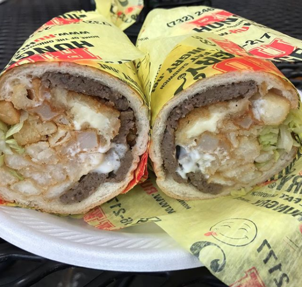 Close-up of a thick burrito-style wrapped sandwich with meat, french fries, lettuce, and condiments