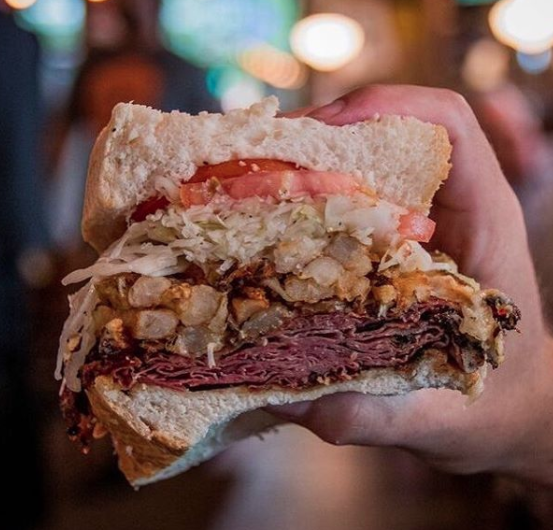 Close-up of a thick roast beef sandwich with fries, lettuce, and tomato