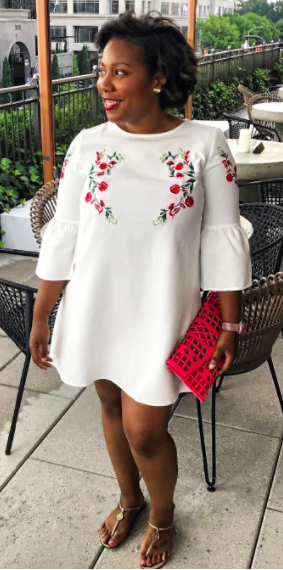 A reviewer wearing the mini dress in white with red floral embroidery