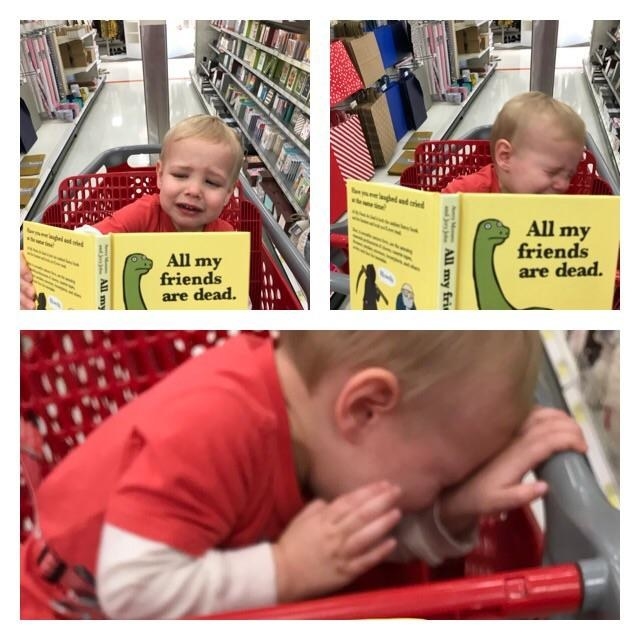 Crying baby sitting in the front of a shopping cart at a store and holding the book &quot;All My Friends Are Dead&quot;